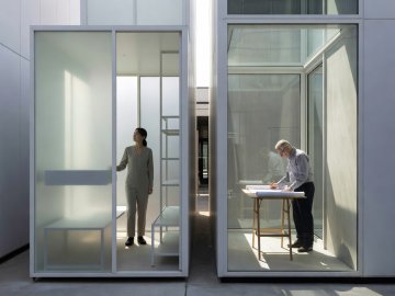Resident standing inside a bright 1.2-metre-wide white steel micro-house with translucent walls