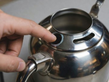 Person pointing to the internal steam pipe opening inside the top rim of a stainless steel kettle