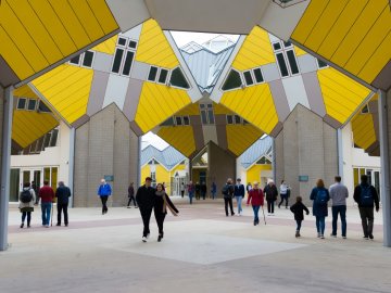 Pedestrians walking across the elevated plaza beneath Piet Blom's yellow tilted Cube Houses in Rotterdam